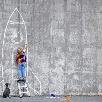 Dream Big Little boy drawing a huge rocket on the wall.