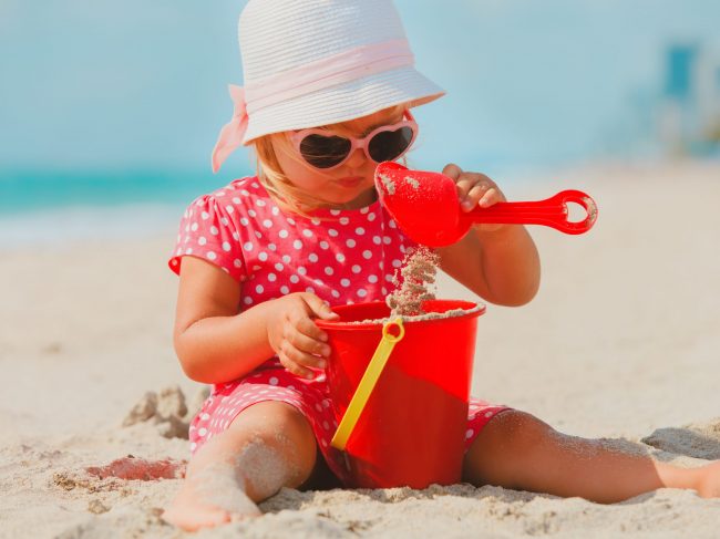 cute little girl play with sand and toys on beach